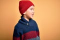 Young little boy kid wearing wool cap and winter sweater over yellow isolated background looking away to side with smile on face, Royalty Free Stock Photo