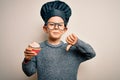 Young little caucasian cook kid wearing chef uniform and hat cooking cupcake with angry face, negative sign showing dislike with Royalty Free Stock Photo