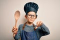 Young little caucasian cook kid wearing chef uniform and hat cooking using wooden spoon with angry face, negative sign showing Royalty Free Stock Photo