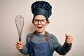 Young little caucasian cook kid wearing chef uniform and hat using manual whisk screaming proud and celebrating victory and Royalty Free Stock Photo