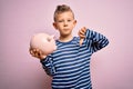 Young little caucasian kid banking money on piggy bank as wealth savings over pink background with angry face, negative sign Royalty Free Stock Photo