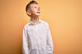 Young little caucasian kid with blue eyes wearing elegant white shirt over yellow background looking away to side with smile on Royalty Free Stock Photo