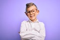 Young little caucasian kid with blue eyes wearing glasses and white shirt over purple background happy face smiling with crossed Royalty Free Stock Photo