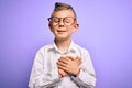 Young little caucasian kid with blue eyes wearing glasses and white shirt over purple background smiling with hands on chest with Royalty Free Stock Photo