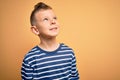 Young little caucasian kid with blue eyes wearing nautical striped shirt over yellow background looking away to side with smile on Royalty Free Stock Photo