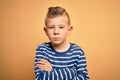 Young little caucasian kid with blue eyes wearing nautical striped shirt over yellow background skeptic and nervous, disapproving Royalty Free Stock Photo