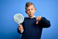 Young little caucasian kid eating sweet candy lollipop over blue isolated background with angry face, negative sign showing