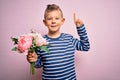Young little caucasian kid holding romantic and cute bouquet of flowers over pink background surprised with an idea or question