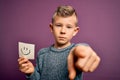 Young little caucasian kid showing smiley face on a paper note as happy message pointing with finger to the camera and to you, Royalty Free Stock Photo