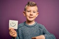Young little caucasian kid showing smiley face on a paper note as happy message with surprise face pointing finger to himself Royalty Free Stock Photo