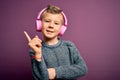 Young little caucasian kid wearing headphones listening to music over purple background with a big smile on face, pointing with Royalty Free Stock Photo