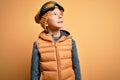 Young little caucasian kid wearing snow glasses and winter coat over yellow background looking away to side with smile on face, Royalty Free Stock Photo