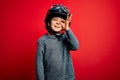 Young little caucasian kid wearing vintage biker motorcycle helmet and googles over red background doing ok gesture with hand Royalty Free Stock Photo