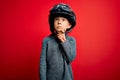 Young little caucasian kid wearing vintage biker motorcycle helmet and googles over red background with hand on chin thinking Royalty Free Stock Photo