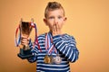 Young little caucasian kid wearing winner medals and victory award trophy over yellow background cover mouth with hand shocked