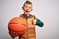 Young little caucasian sports kid playing basketball holding orange ball over isolated background happy with big smile doing ok