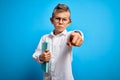 Young little caucasian student kid wearing smart glasses and holding a book from school pointing with finger to the camera and to