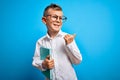 Young little caucasian student kid wearing smart glasses and holding a book from school pointing and showing with thumb up to the