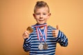 Young little caucasian winner kid wearing award competition medals over yellow background happy with big smile doing ok sign,