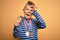 Young little caucasian winner kid wearing award competition medals over yellow background with happy face smiling doing ok sign