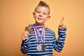 Young little caucasian winner kid wearing award competition medals over yellow background surprised with an idea or question
