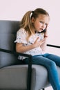 Young little confused girl talk phone sit on chair isolated on white background