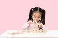 Young little cute asian girl build a house from wooden block construction, wood toy, jenga house on desk in isolated pink Royalty Free Stock Photo