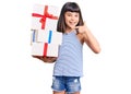 Young little girl with bang holding gifts smiling happy pointing with hand and finger