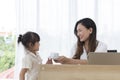 Young little girl bring cup of coffee to her mother, while young mother working on desk using laptop computer during work from hom Royalty Free Stock Photo