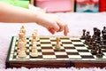 Young little girl, child playing chess, chessboard side view, hand moving a chess piece, about to grab it, closeup. Making a move