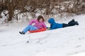 Young little girl enjoying sledding outside on a snow day while her brother holds onto the back dragging along after her Royalty Free Stock Photo