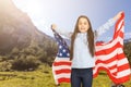 Young little girl holding American flag on amazing sky, mountain and meadow nature background at sunset. Royalty Free Stock Photo