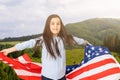 Young little girl holding American flag on amazing sky, mountain and meadow nature background at sunset. Royalty Free Stock Photo