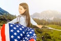 Young little girl holding American flag on amazing sky, mountain and meadow nature background at sunset. Royalty Free Stock Photo