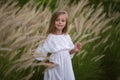 Young little girl with long hair, white dress lonely walking in field and collecting flowers for a bouquet. little girl with a Royalty Free Stock Photo