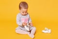 Young little girl in striped dress with pink heart and tights sitting on yellow background in studio and playing with her white Royalty Free Stock Photo