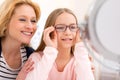 Young little girl trying glasses at the optician w her mother