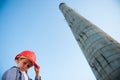 Young little caucasian kid in red helmet near plant factory high pipe on blue sky background with copy space