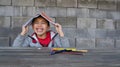 Young little latino boy latino holding a yellow book on his head on brick background with pencils over the desk and having fun and Royalty Free Stock Photo