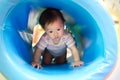 Young little smiling Asian baby enjoy playing and crawling in blue tube at kid playground. Royalty Free Stock Photo