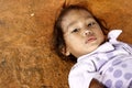 Young little street girl looks at the camera while lying down on a pavement.