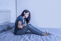 Young lonely beautiful and sad latin woman at home suffering period pain or feeling sick and depressed sitting on bed helpless in Royalty Free Stock Photo