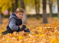 Boy sitting in brown fall leaves with skateboard. Royalty Free Stock Photo