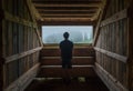 Young lonely teenage boy standing near the wooden forest house window and enjoying the morning spruce foggy forest. Traveling and Royalty Free Stock Photo