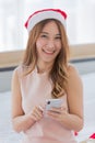 A young long brown hair female wearing red and white christmas hat and pink sleeveless dress using her silver mobile phone while Royalty Free Stock Photo