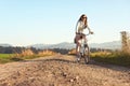 Young long hair woman with sunglasses riding bike on dusty country road, afternoon sun lit country background Royalty Free Stock Photo