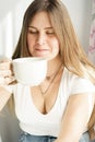 A young long-haired blond woman in a white T-shirt is drinking tea Royalty Free Stock Photo