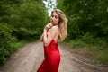 Young long-haired girl in a red dress posing in a summer park on the road. Women`s beauty, lifestyle, fashion