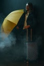 Young long haired man holding yellow umbrella and suitcase Royalty Free Stock Photo