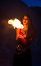 Young long-haired woman in a red top and ethnic necklace holds on handbreadth two small torch and blowing on the fire